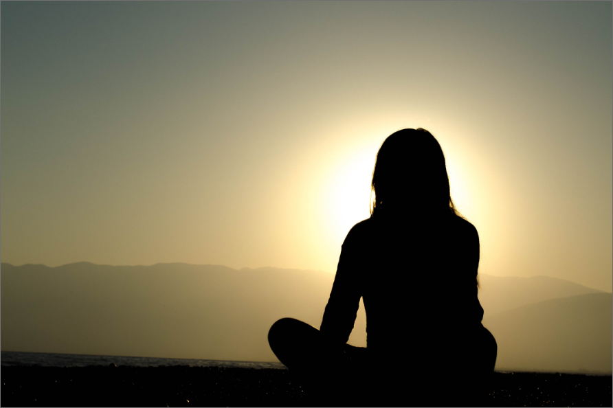 Woman meditating in front of morning sunrise